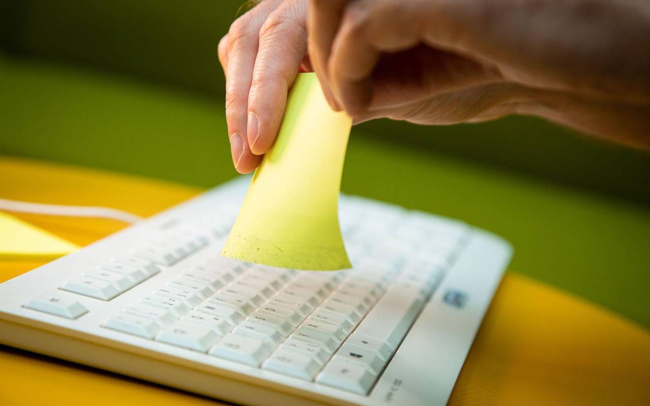 Mann nutzt zum Reinigen der Tastatur einen Klebezettel