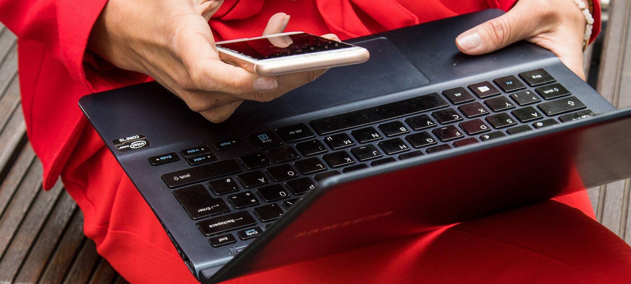 Eine Frau hält ein Smartphone und ein Laptop in den Händen