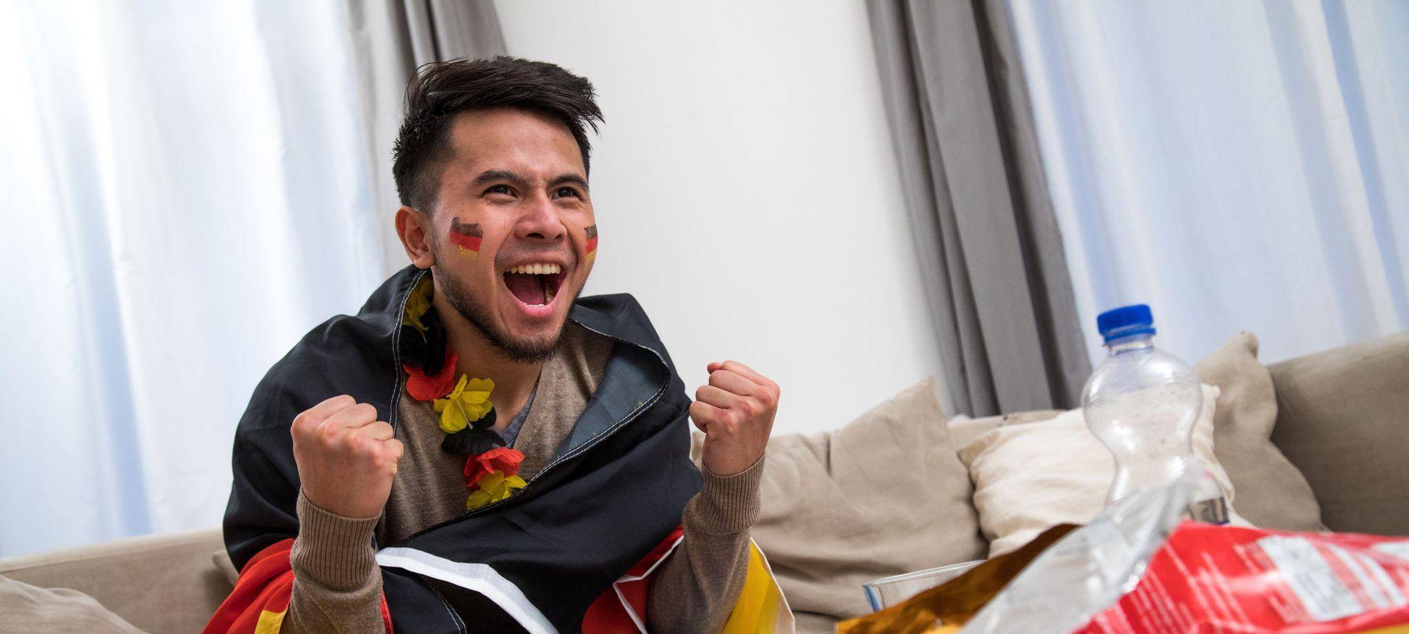 Ein Mann fiebert in WM-Deko vor dem Fernseher mit