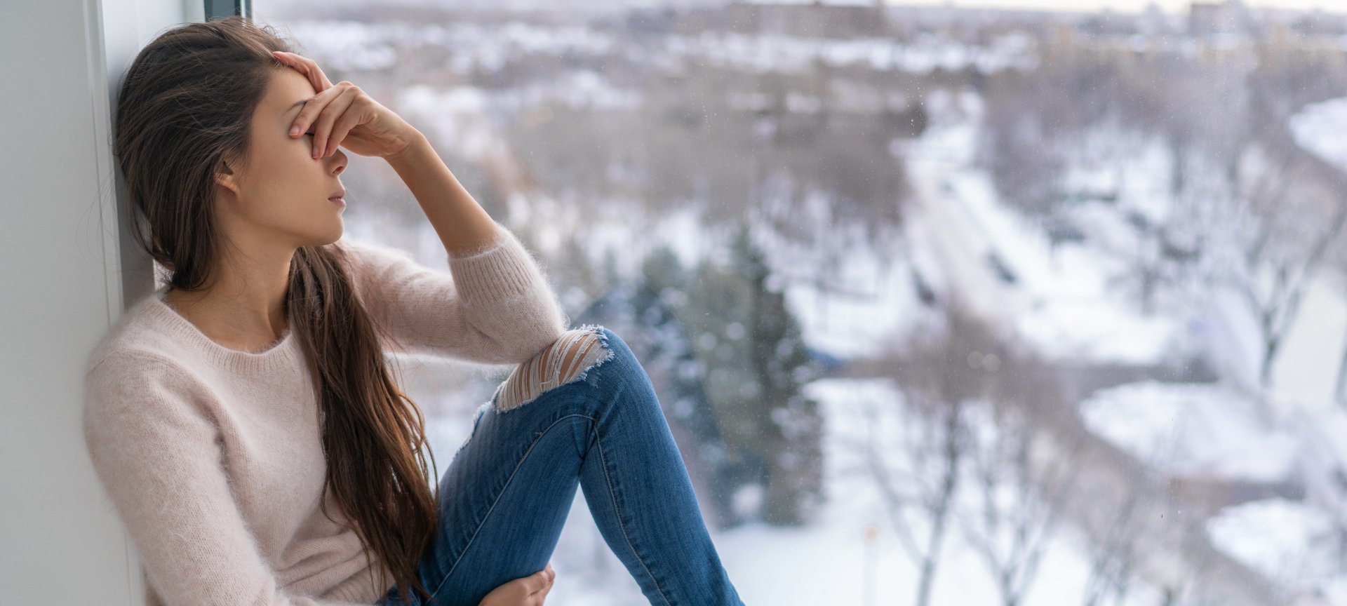 traurige Frau sitzt am Fenster und schaut in die kalte Winterlandschaft